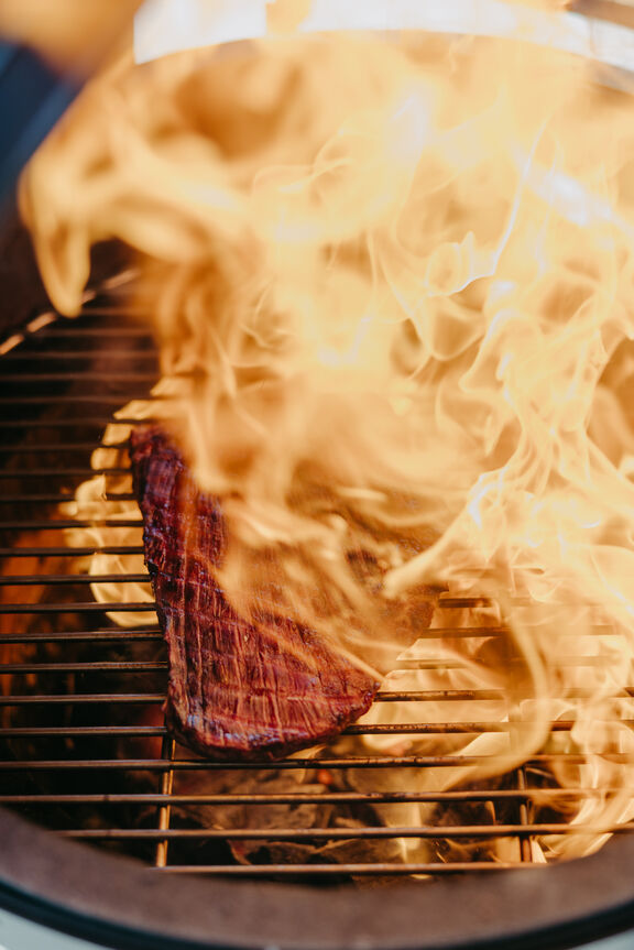 Griller an Strandbar Hohe Flamme in einem Griller auf dem ein Stück Fleisch liegt
